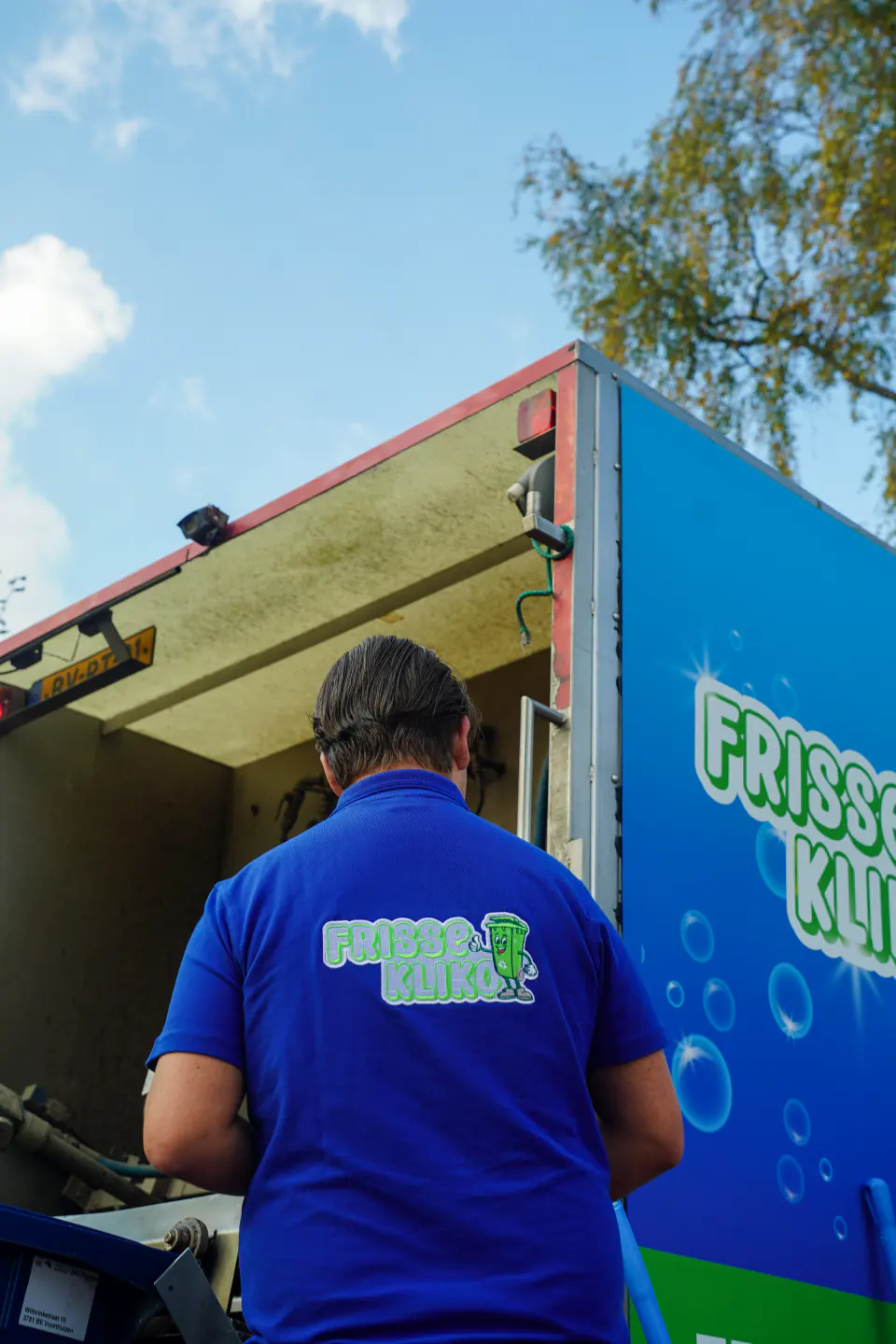 Medewerker van Frisse Kliko staat bij de open achterzijde van de reinigingswagen.